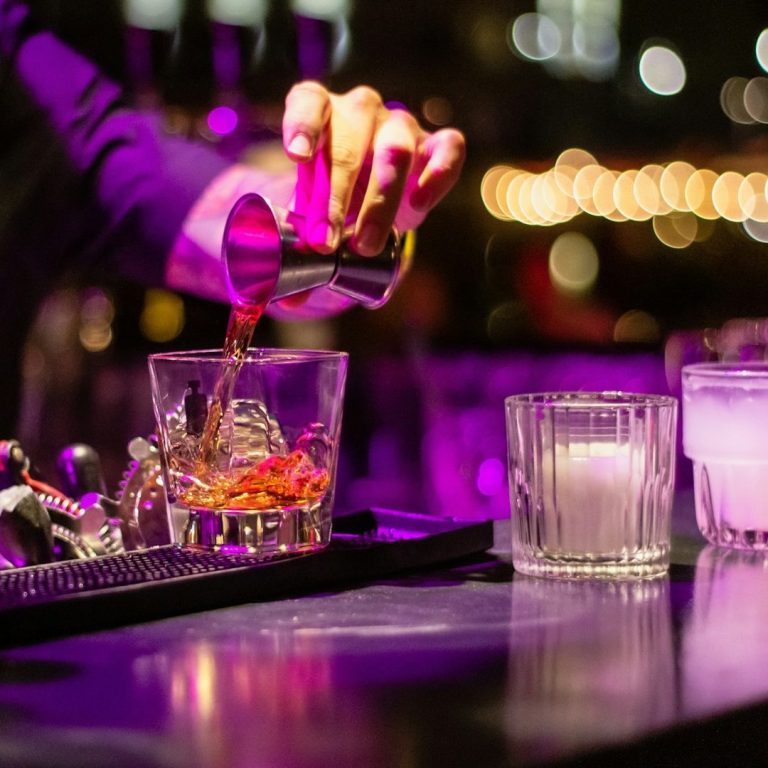 Ein Barkeeper gießt ein Getränk in ein Glas mit Eiswürfeln. Ambiente mit gedämpftem Licht. Club, Kneipe, Pub in Duisburg.