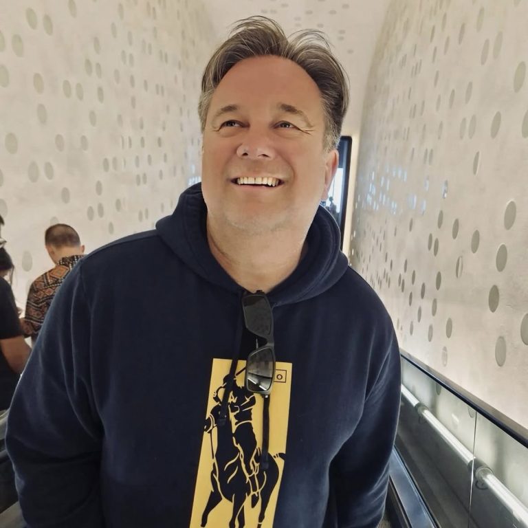 Lächelnder Mann in einem blauen Hoodie, steht in einem modernen Innenraum. Dirk Hartkopf, Moderator für EDEKA, Audi, METRO, REWE uvm.