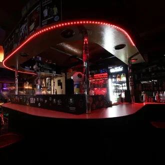 Dunkle Bar mit rohen LED-Lichtern und beleuchtetem Getränkeangebot im Hintergrund.