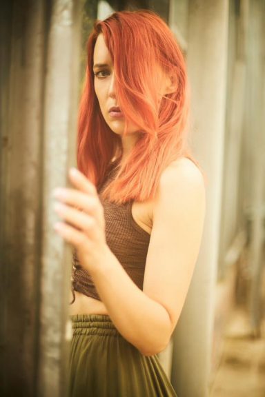 Junge Frau mit roten Haaren in einem grünen Rock in einer urbanen Umgebung.